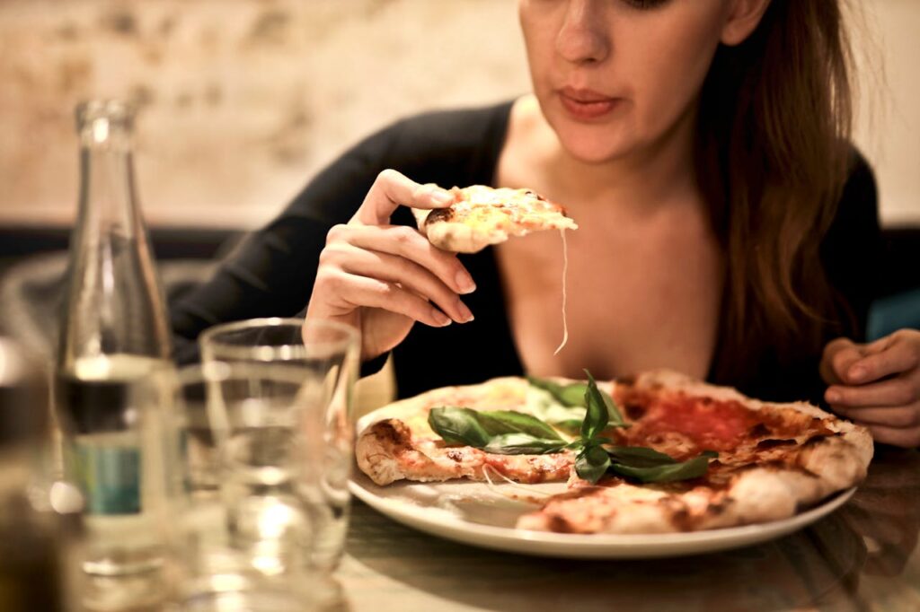 Kobieta jedząca pizzę, która może wywołać uczucie ciężkości po jedzeniu porady dietetyczne.